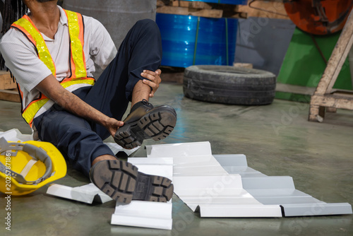 An industrial male engineer injured his leg in an accident at an industrial worksite, lying on floor at manufacturing factory. An injured man worker at workplace feeling in pain and need help.