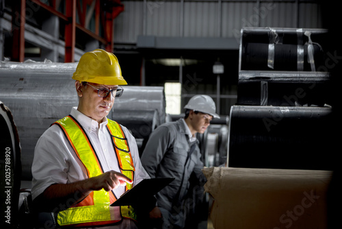 Cuadro en lienzo Senior worker with tablet inspecting large metal sheet coil at factory during night shift