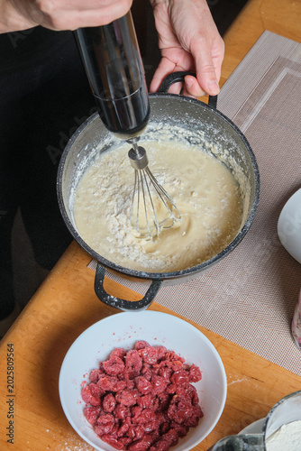 Skilled baker stirs creamy berry batter. Warm kitchen scene capturing hands mixing smooth batter with juicy raspberries
