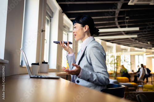 Foto Businesswoman talking on smartphone using speakerphone feature, working at co-wo