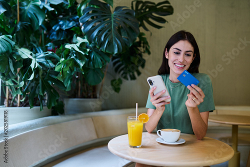 Young woman using credit card for online shopping on her phone drinking coffee in caffee cafeteria