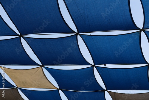Geometric pattern of blue and tan shade sails against a clear sky