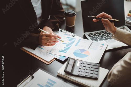 Business professionals analyzing financial reports, reviewing charts and graphs, and collaborating on strategic planning during a meeting, with a laptop and calculator on the desk