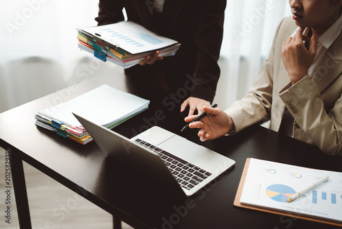 Two professionals collaborating in an office, reviewing financial charts and reports on a laptop, discussing strategy and planning project development and growth