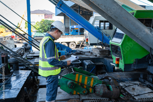 Photos Engineer reviews a crane inspection checklist on a mobile crane deck, checking wire rope and hoist components to support safety, maintenance, and lifting readiness