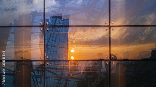 Abstract reflection of sunset sky on modern glass curtain wall building with interior structure (Golden hour sunset reflected in the glass facade of an urban skyscraper)