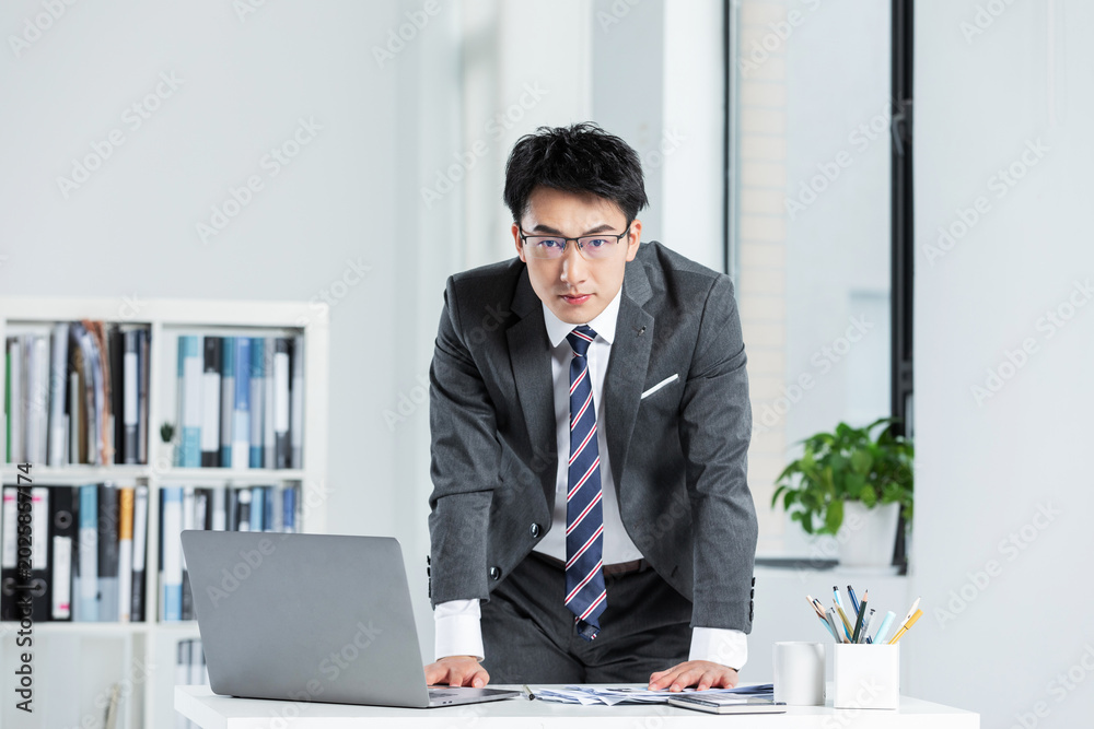Naklejka premium Confident businessman working with laptop and documents in modern office