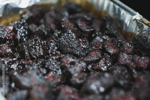 Pork Belly Burnt Ends cooked until black on a pellet grill smoker. The delicious morsels of fatty pig meat are resting in a tinfoil pan ready to eat for dinner. 