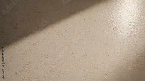 Close up of a rough concrete wall texture with a diagonal shadow cast across the grey cement surface