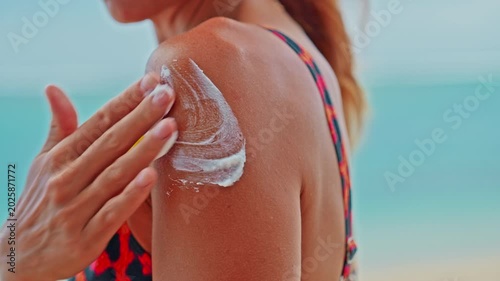 Young woman applying moisturizing sunscreen lotion on a shoulder with a beautiful ocean in the background. Skin care sun protection. Closeup