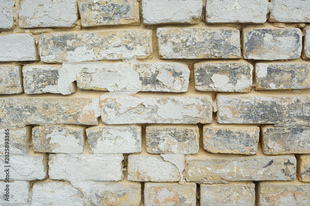 Fototapeta premium Weathered brick wall with peeling white paint, showing aged texture and rough surface detail.