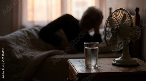 Elderly man resting in bed with a fan and glass of water on bedside table