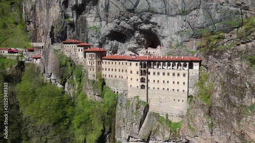 Close-up aerial view of Sumela Monastery complex in Turkey. Drone panning across the multi-story stone building and dark mountain cave opening carved into the sheer cliff side