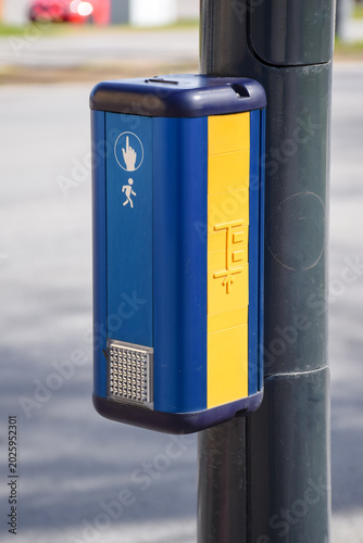 Blue and yellow pedestrian crossing request button mounted on a pole at a crosswalk in an urban street environment