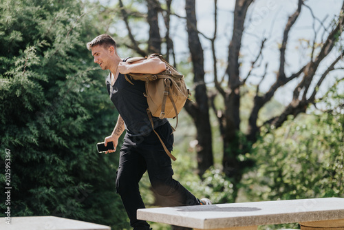 Foto A young man runs carrying a backpack and smartphone in a leafy outdoor area