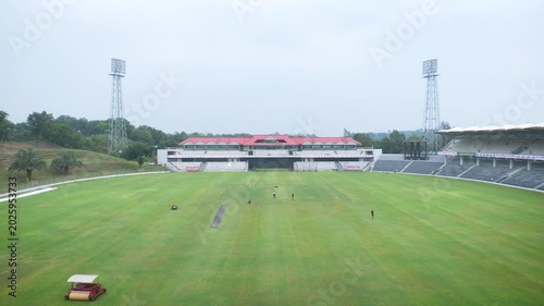 High angle establishing shot of a massive empty cricket stadium with floodlight towers and green field