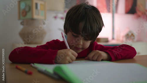 Photography Young boy sitting at desk writing in notebook with pencil, focused child concent