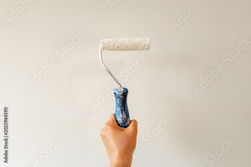 Hand holding paint roller applying white paint on interior wall