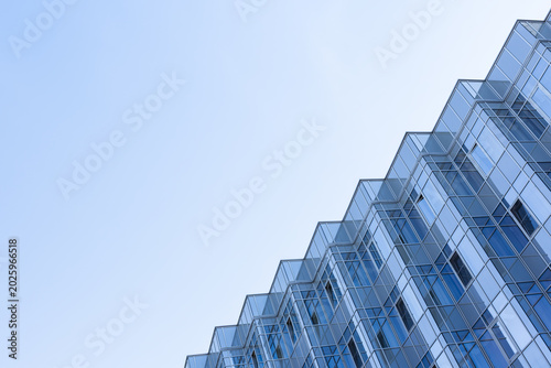 Modern glass office building facade photographed from an upward angle, showcasing repeating geometric patterns, reflective blue windows and minimalist corporate architecture against a clear sky