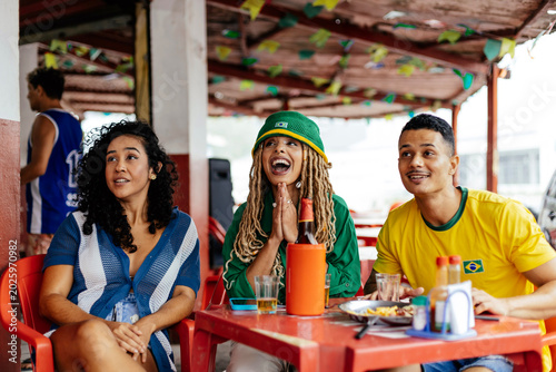 Brazilian friends reacting while watching football together at a casual bar.