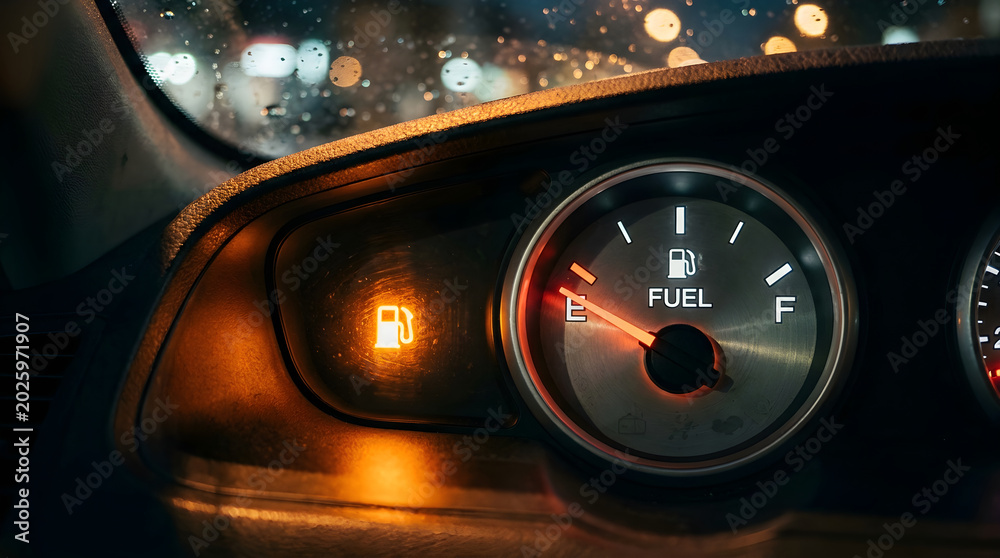 Obraz premium Analog car dashboard fuel gauge showing empty tank and glowing low fuel warning light at night