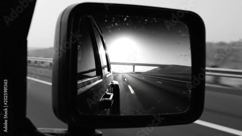 Black and white view from side mirror of a car driving on a highway with a bridge ahead