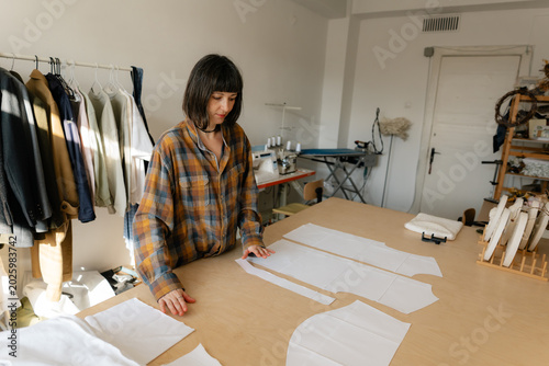 Fashion designer arranging paper pattern pieces on table in small sewing studio atelier