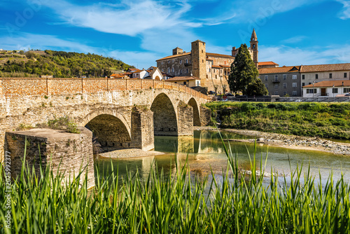 Medieval stone bridge over the river and old town of Monastero Bormida in the background in Italy