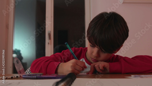 Photography Boy concentrating on small paper card while writing at table, schoolwork scene i