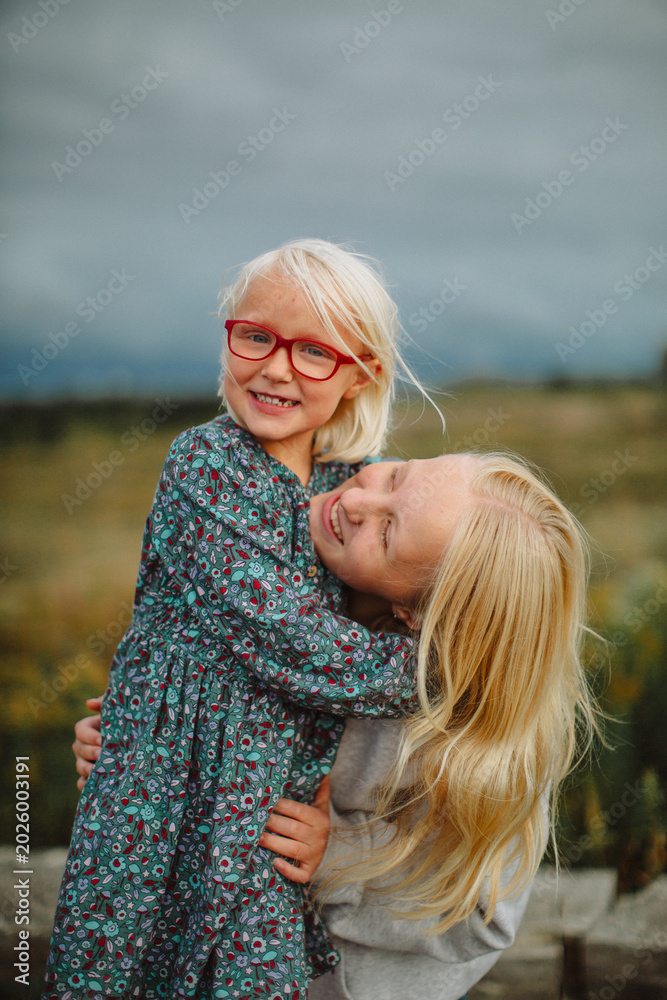 Fototapeta premium Happy sisters hugging outdoors before a storm – candid family lifestyle portrait 