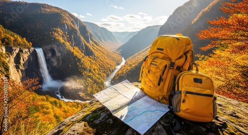 Yellow backpacks and an open paper map rest on a rocky ledge overlooking a massive waterfall in a vibrant golden and red autumn valley, travel, majestic, cliffs