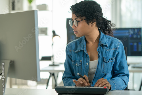 Asian woman coder in glasses typing code for AI analysis. Focused on software development, robotic control, and digital communication in a tech workplace.

