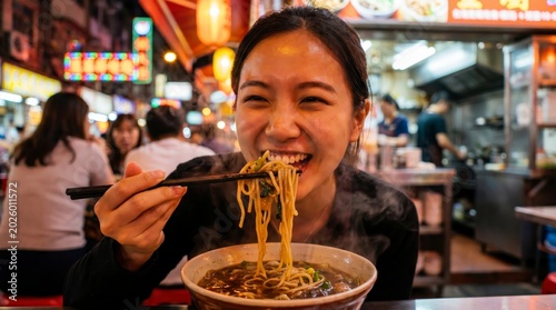A woman enjoys steaming hot ramen noodles at a lively, brightly lit night market or street food stall.