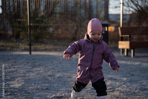Foto smiling toddler in a purple one-piece snowsuit and pink beanie toddling across a