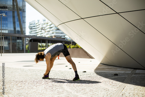 Bild auf Leinwand Man stretches before workout in urban area near modern building in bright sunlig