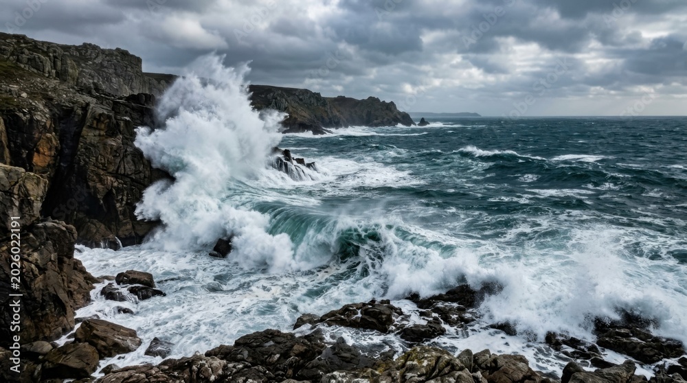 Fototapeta premium Ocean waves crashing against rugged cliffs under dramatic cloudy sky on stormy day at rocky coastal shoreline.