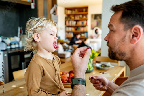 Fotografi Toddler refusing food offered by father at kitchen.