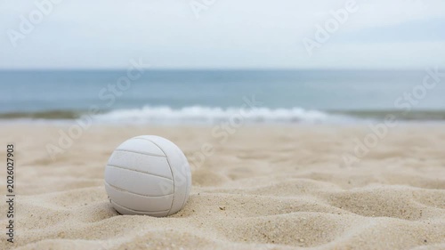 White volleyball nestled in soft sand on a beach with the ocean and sky in the distance Keywords: volleyball, beach, sand, ocean, sea, water, waves, sport, game, recreation, summer, vacation