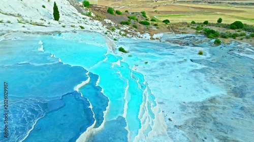 Drone view of Travertines of Pamukkale, Turkey. Turquoise thermal channels, white limestone and green fields create a scenic travel view.
