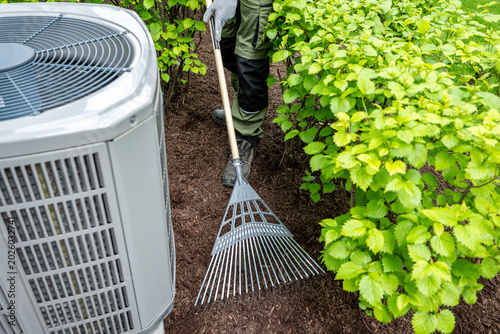 Konstfotografi Landscaper raking fresh mulch around bushes in residential backyard close up to air condition