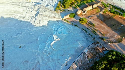 Drone view of Travertines of Pamukkale, Turkey. White mineral terraces, turquoise pools and nearby trees create a natural travel scene.