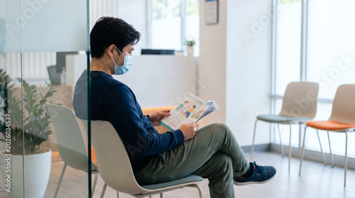 Man Wearing Mask Waiting And Reading In Clinic Lobby