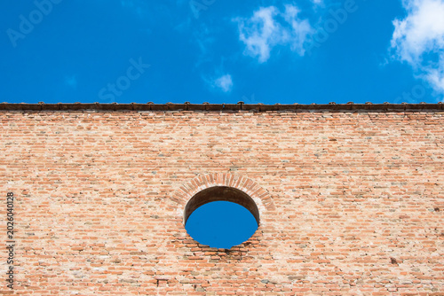 Dettaglio di un muro di mattoni con un  foro circolare ial centro da cui si vede il cielo