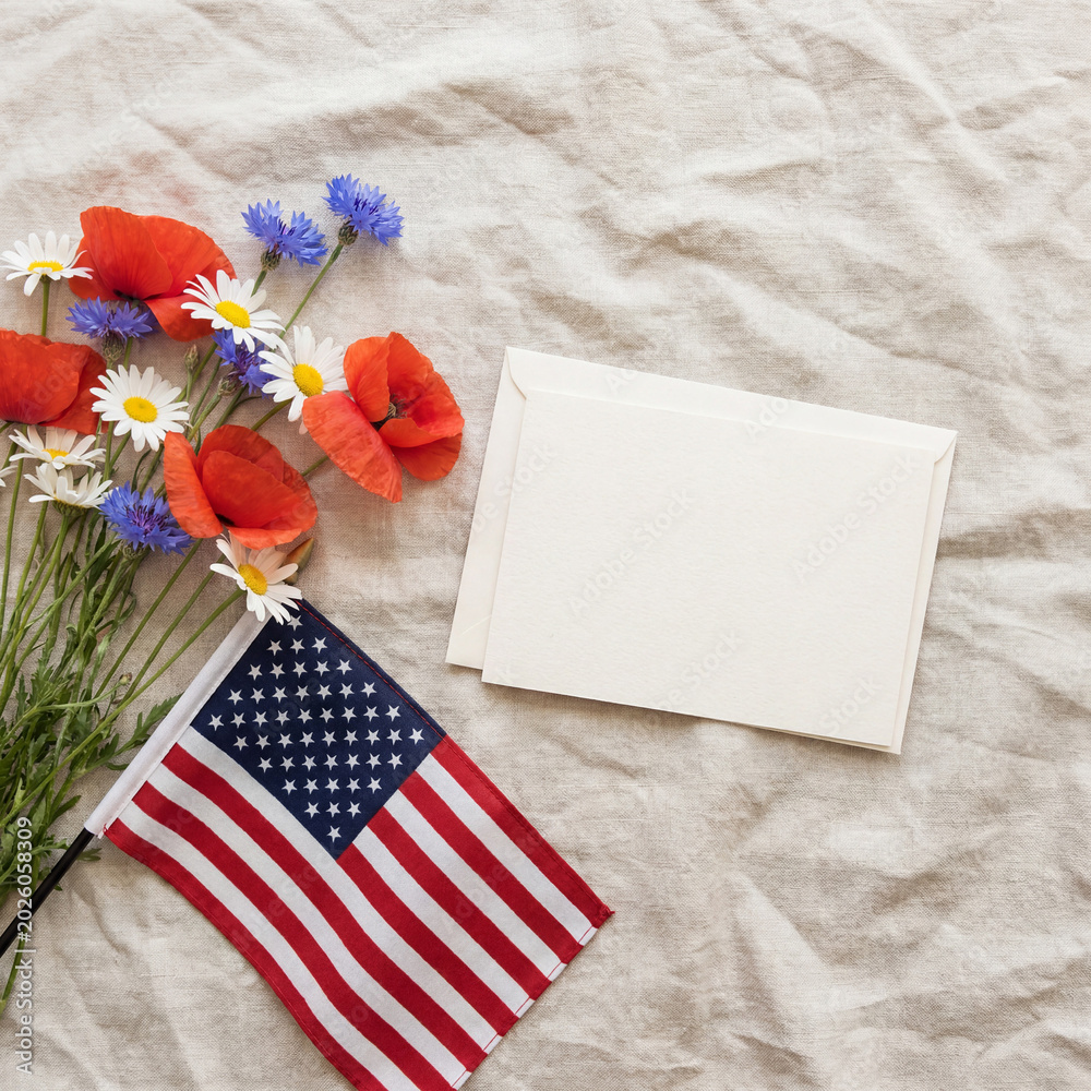 Obraz premium Patriotic flat lay with US flag, spring flowers, and empty greeting card space
