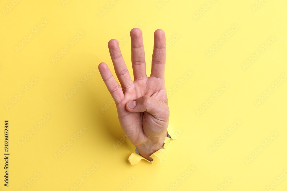 Naklejka premium Man showing number four with fingers through hole in yellow paper, closeup