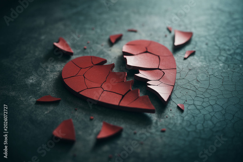 Broken heart symbol shattered into pieces on dark textured background, symbolizing heartbreak, end of love, sadness.