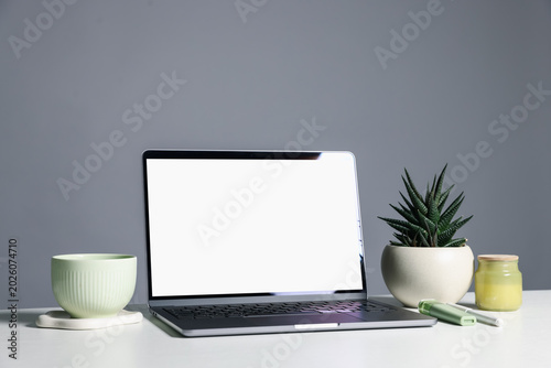 Stylish workplace. Laptop with blank screen, cup and decor on white table against gray background. Space for text