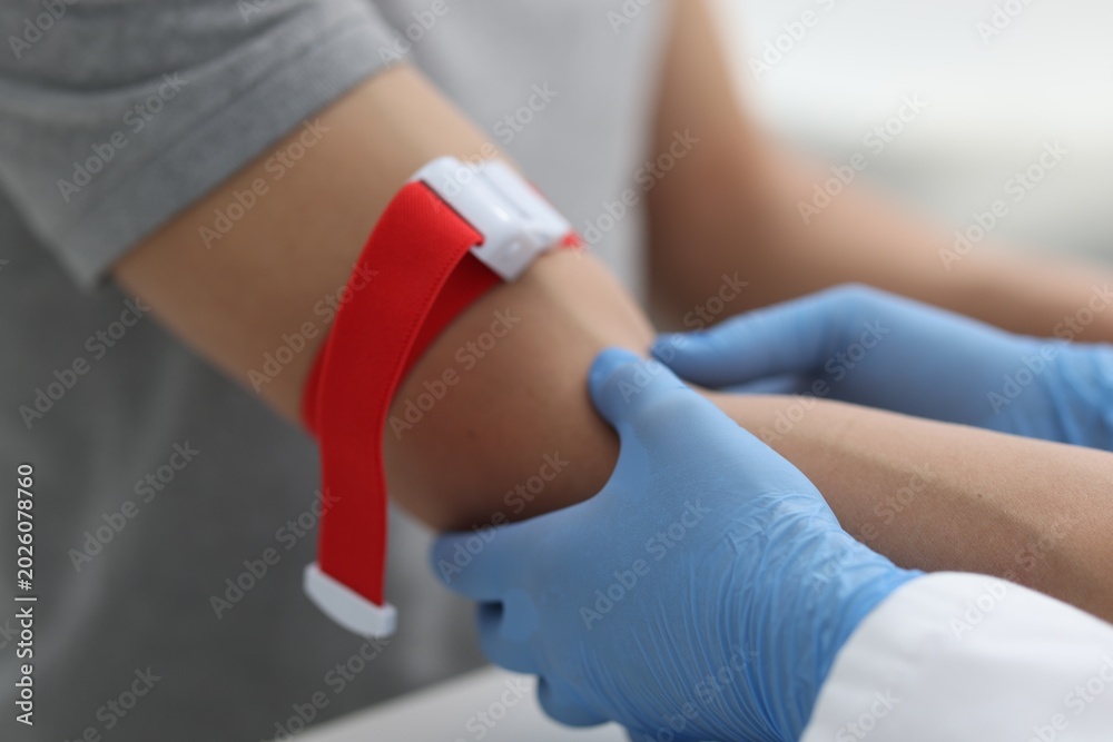 Obraz premium Nurse palpating patient's vein before drawing blood sample at table in clinic, closeup