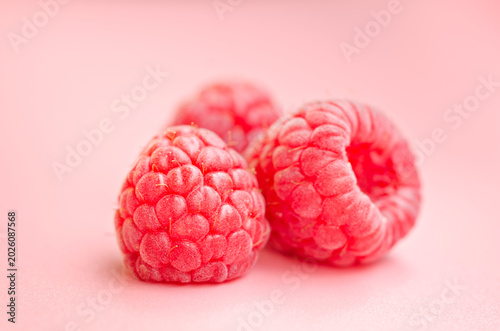 Three fresh raspberries close up on pink background