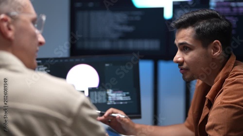 Close up of software developers sitting at an office desk to discuss machine learning code scripts and system architecture changes on a desktop monitor.